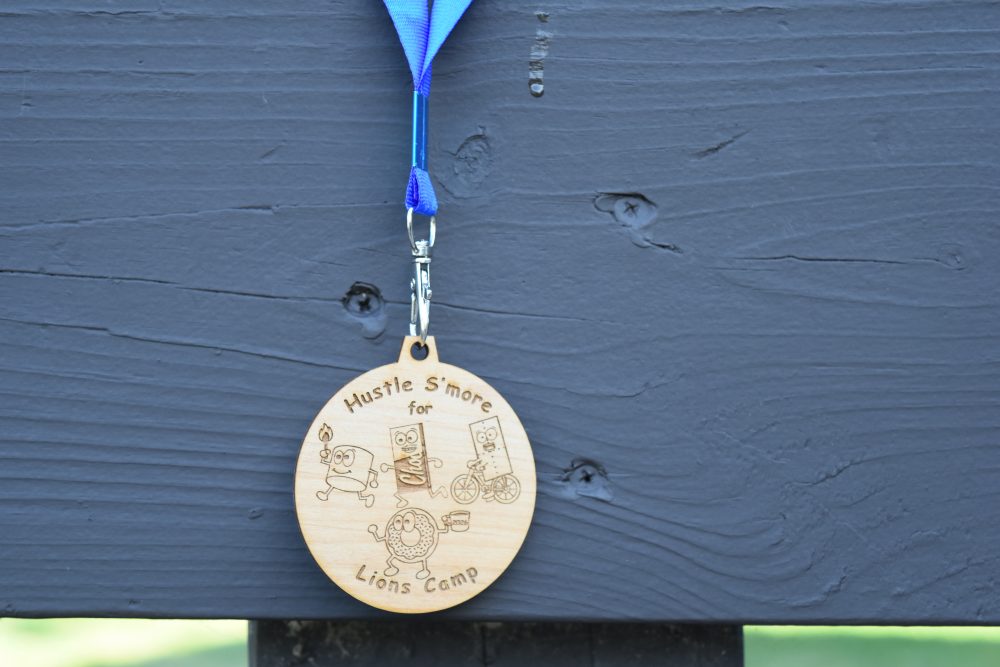 Image of 2026 Medal for First Place, a wooden disc featuring a marshmallow, chocolate bar, graham cracker, and donut